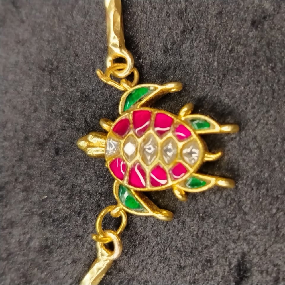 Golden turtle pendant with colorful Kemp stones on a dark gray background