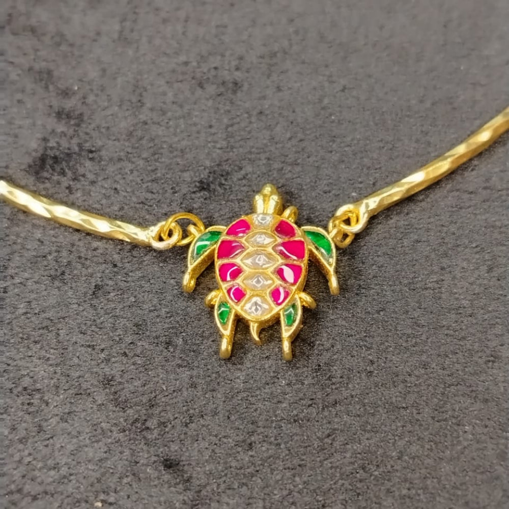 Golden turtle-shaped pendant with red and green Kemp stones on a dark surface