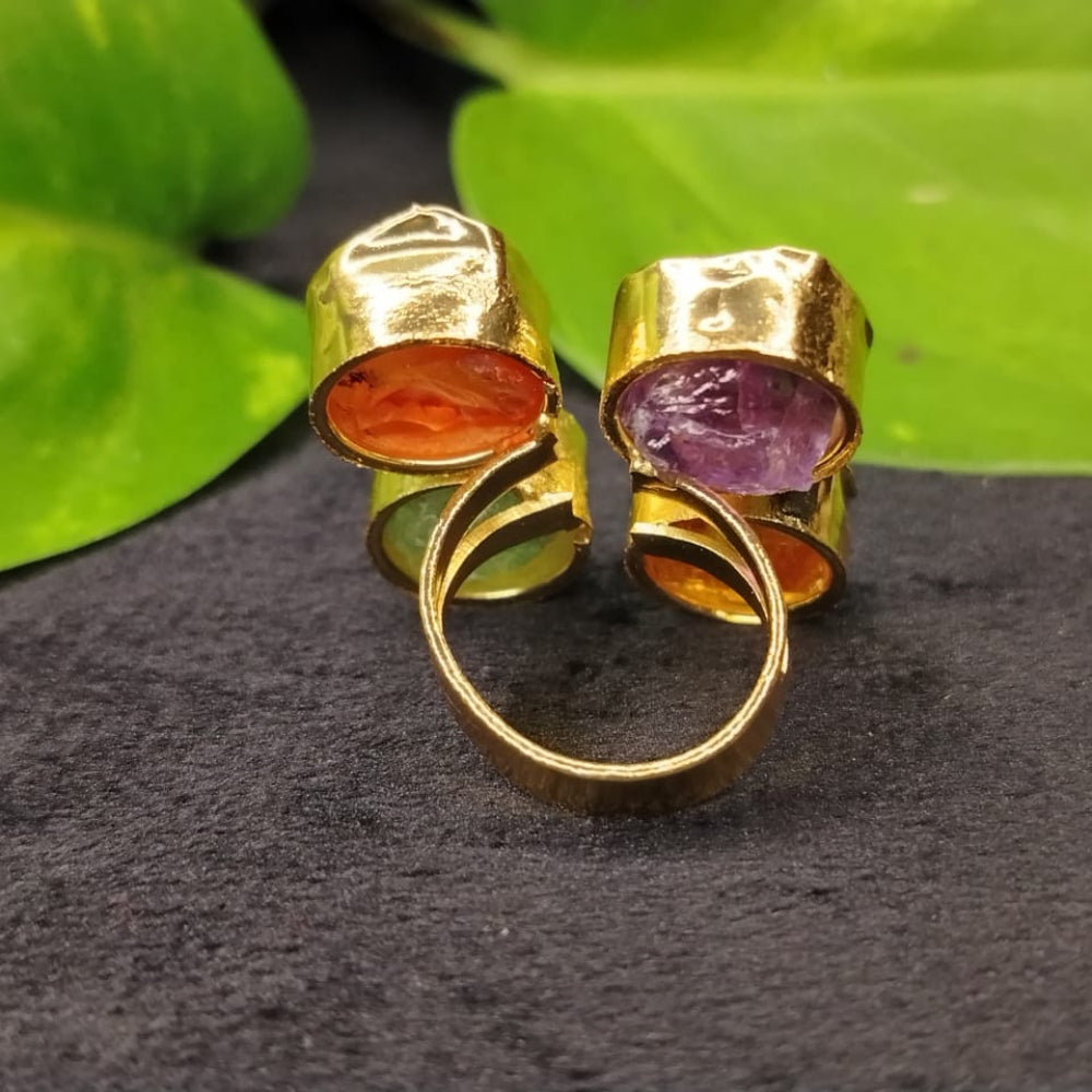 Gold ring with multicolored gemstones on a dark surface with green leaves in the background