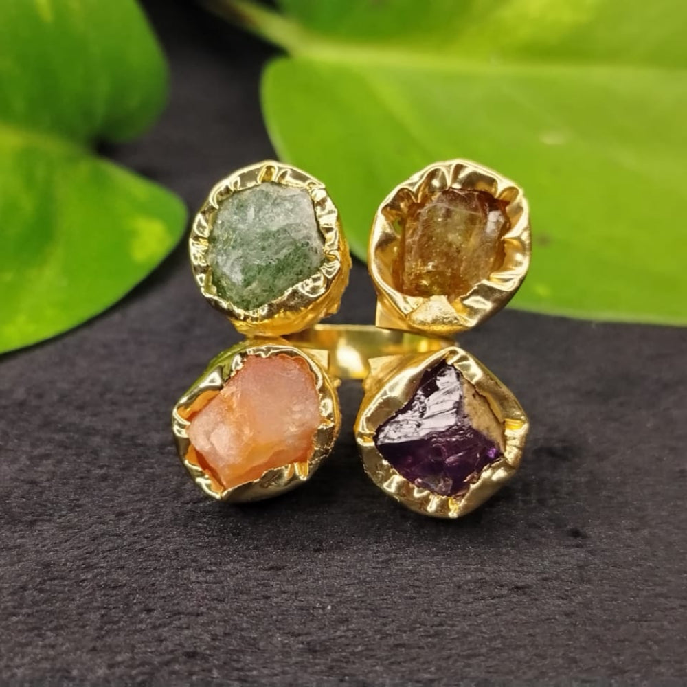 Gold earrings with multicolored gemstones on a dark surface with green leaves in the background