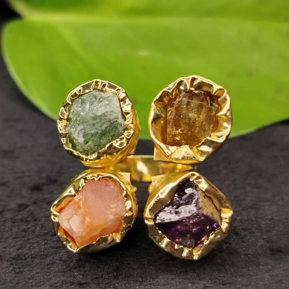 Gold earrings with multicolored gemstones on a dark surface with green leaves in the background