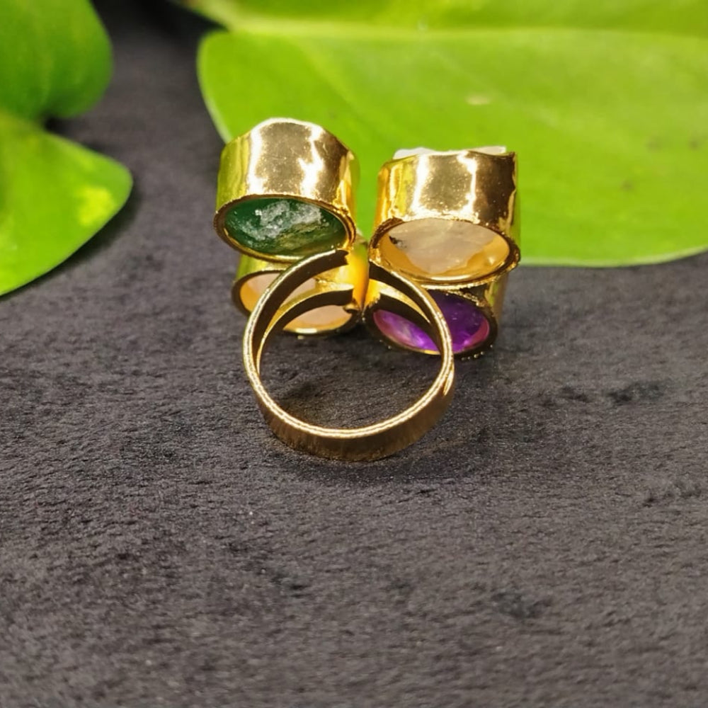 Gold ring with gemstones on a dark surface with green leaves in the background