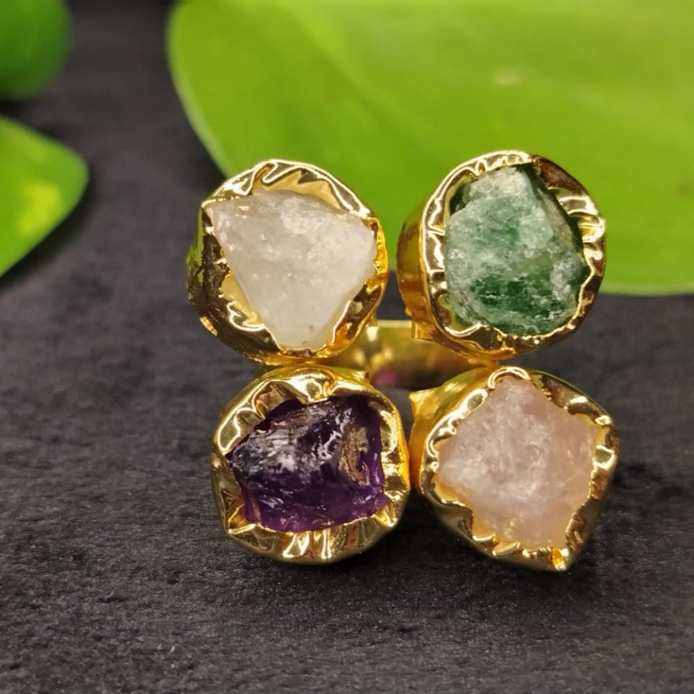 Gold ring with four gemstones on a dark surface with green leaves in the background
