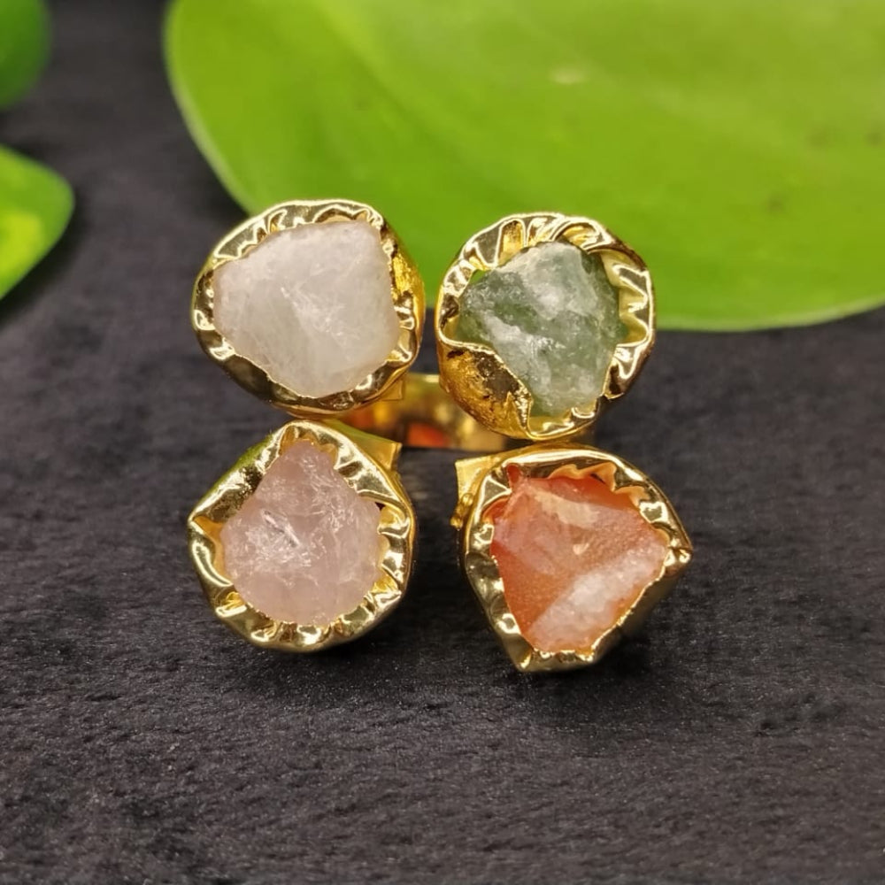 Gold-framed earrings with multicolored stones on a dark surface with green leaves in the background