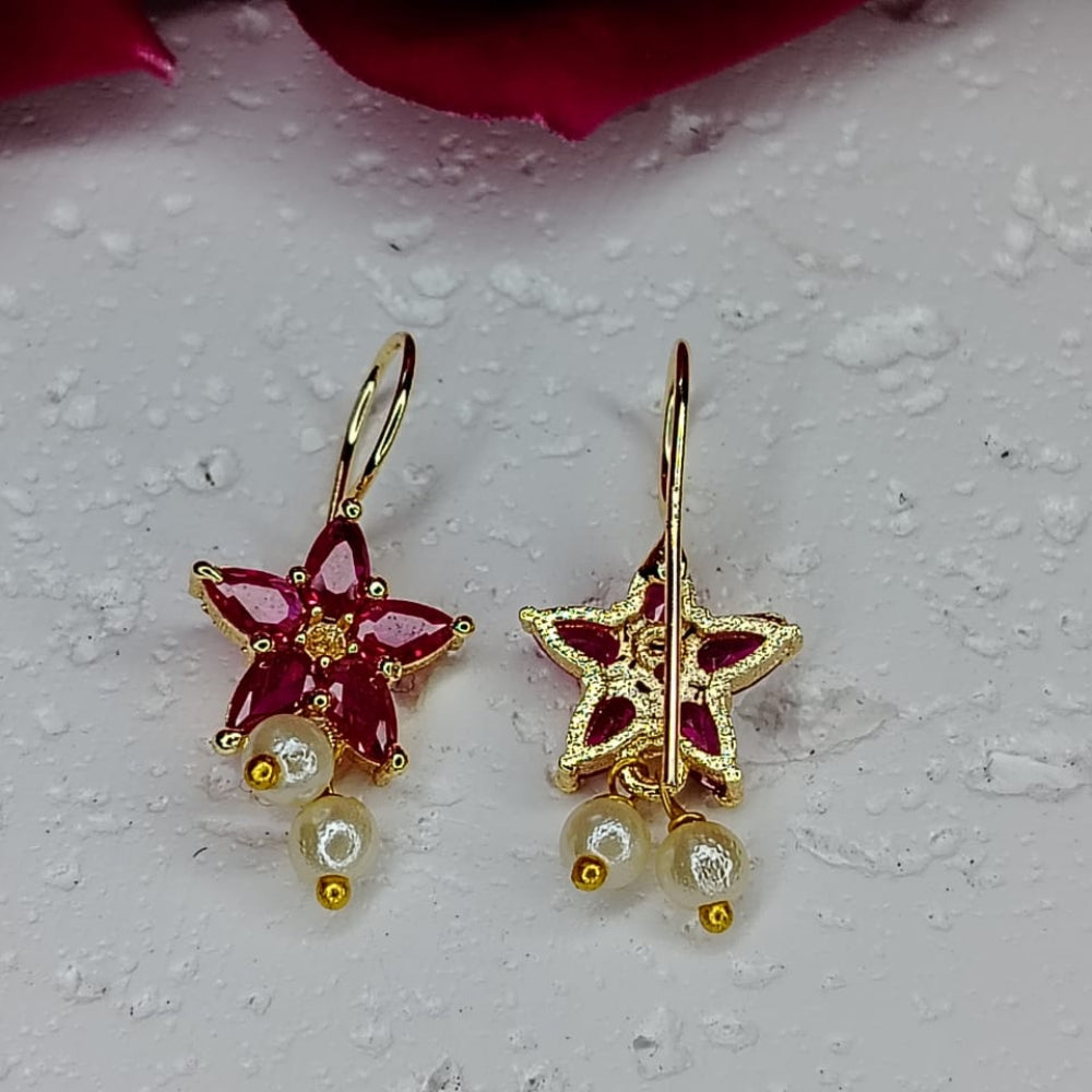 Gold ear cuffs with red gemstones and pearl-like beads on a textured white surface.