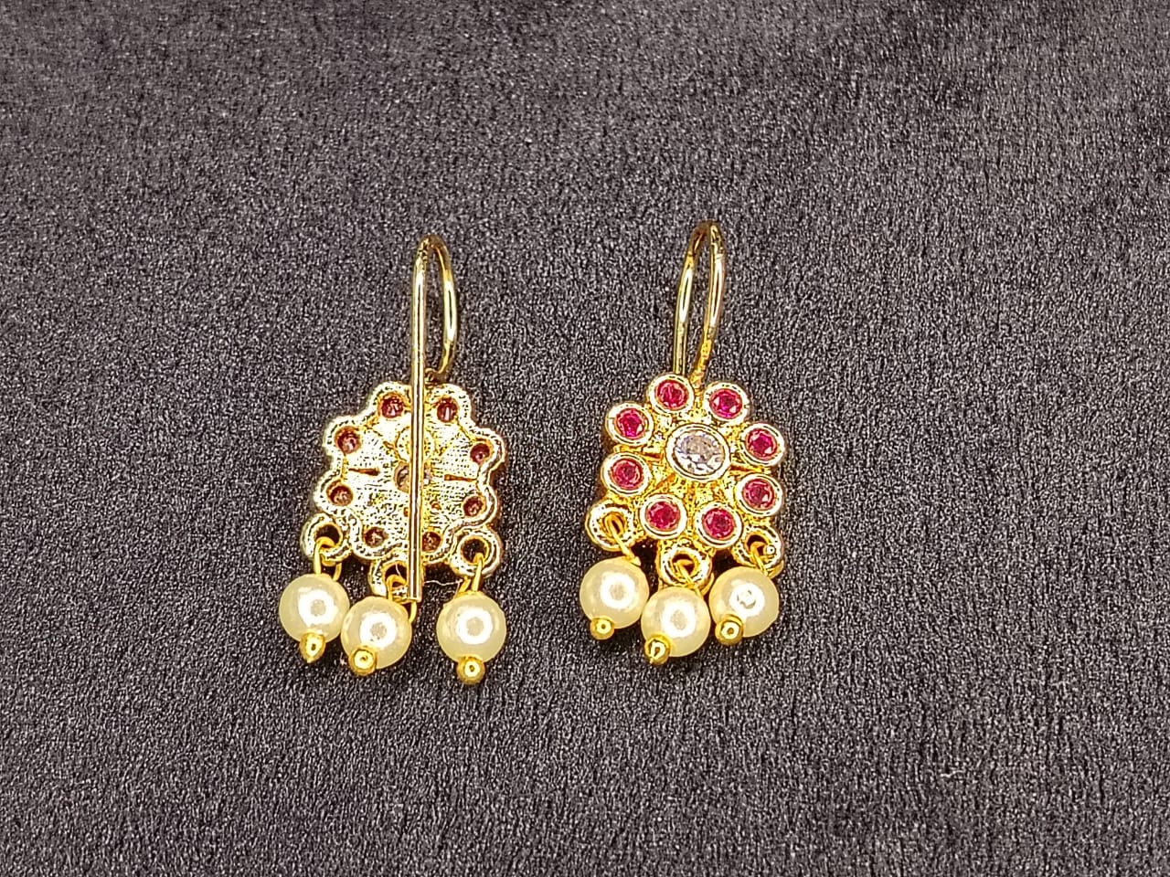 Gold earrings with pearls and red stones on a gray background
