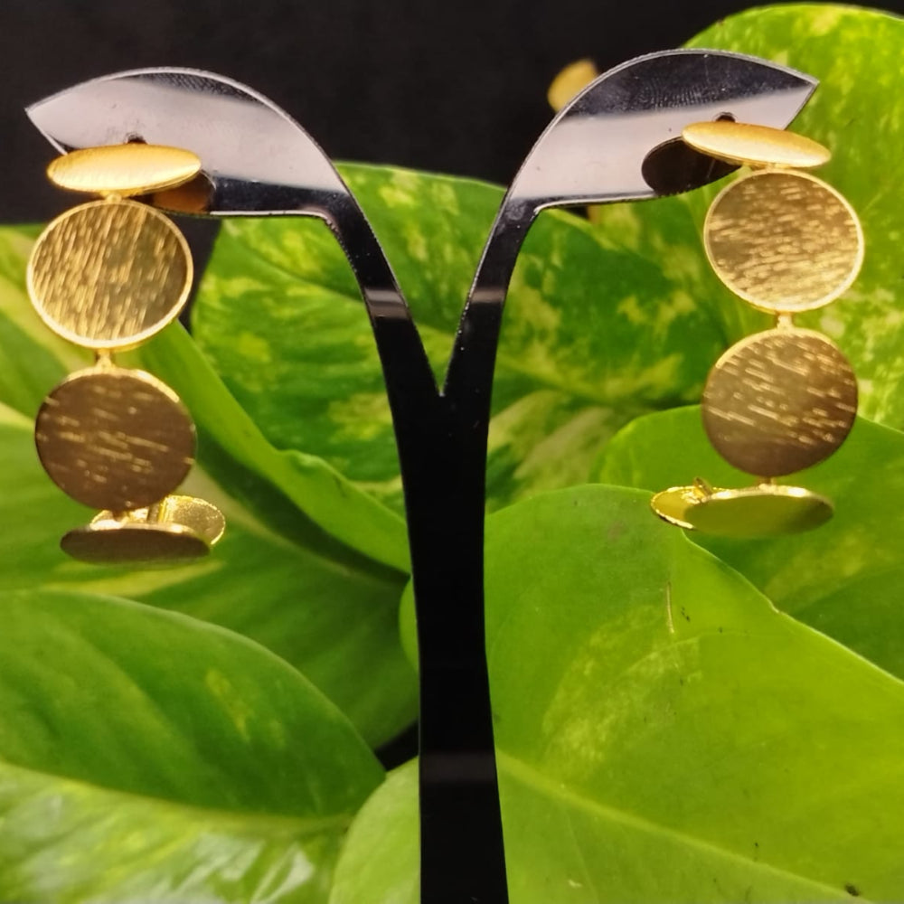 Golden earrings on a stand with green leaves in the background