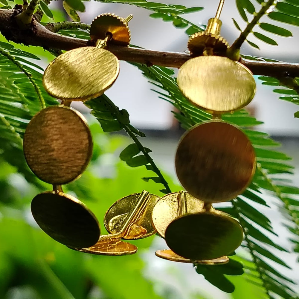 Gold earrings hanging from a branch with green leaves
