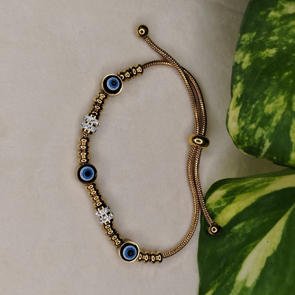Gold bracelet with blue eye beads on a beige surface with a green leaf