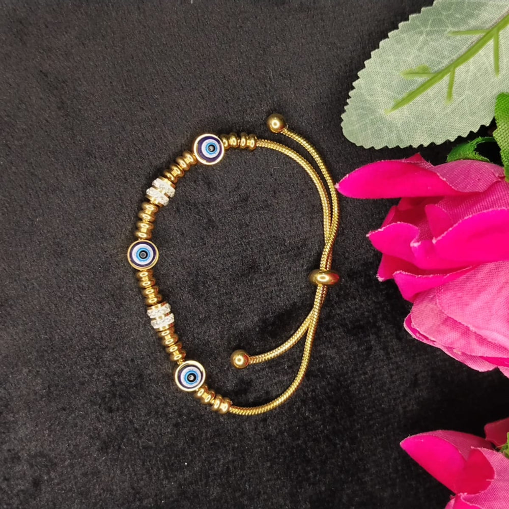 Gold bracelet with blue and white beads on a black surface with pink flowers.