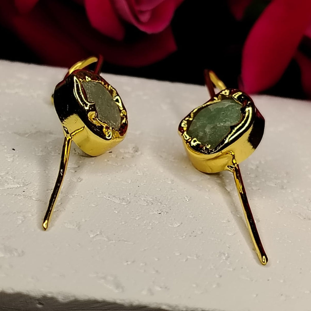 Gold earrings with green stones on a white surface with pink flowers in the background
