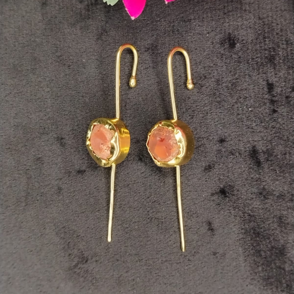 Gold earrings with coral stones on a dark surface with pink flowers.