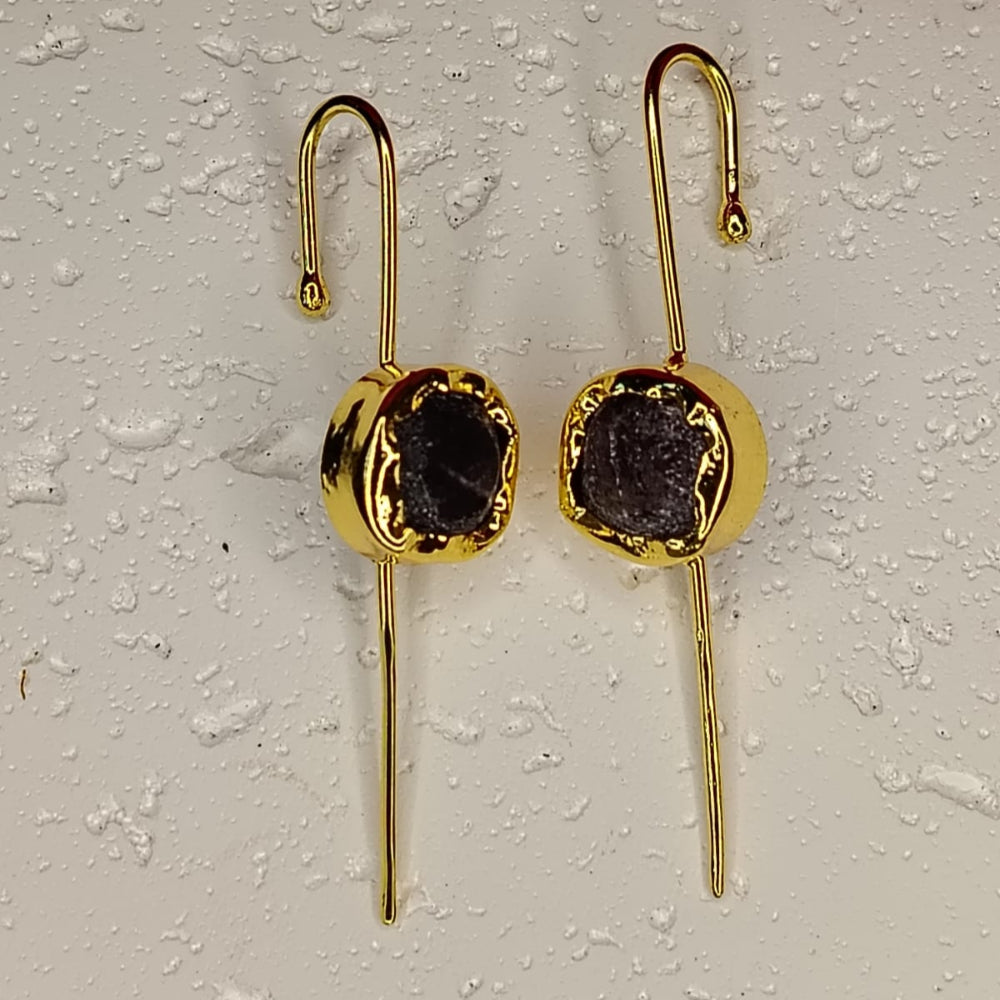 Gold earrings with dark gemstones on a textured white surface.