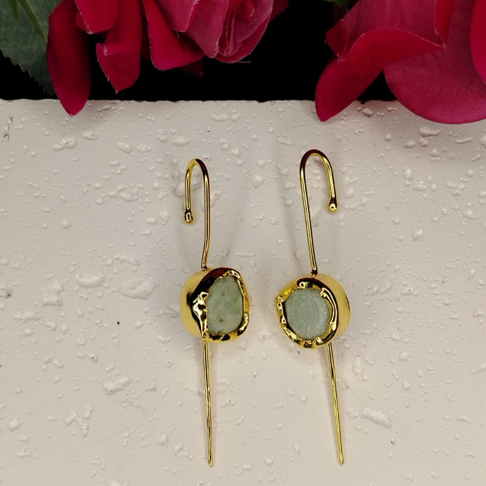 Two gold bugadi earrings with green stones on a textured white surface