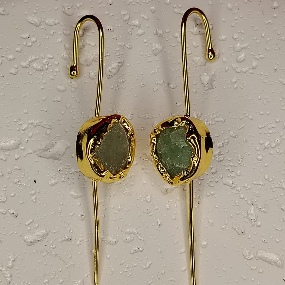 Gold earrings with green gemstones on a textured white surface