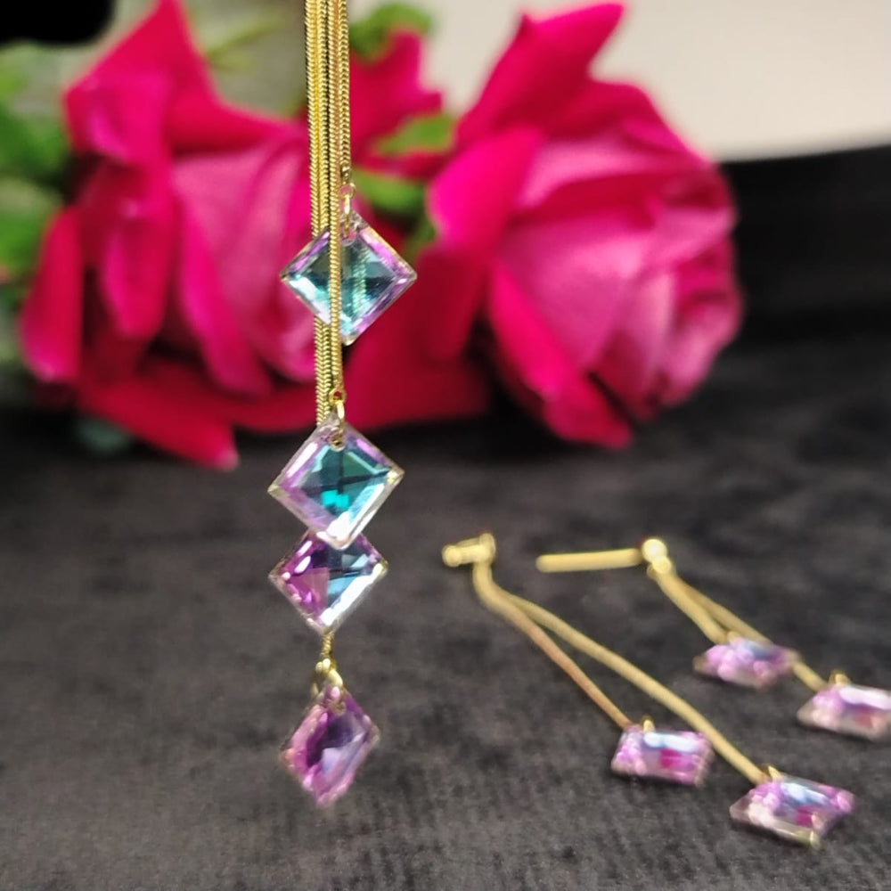 Gold earrings withrainbow crystal gemstones in front of pink flowers