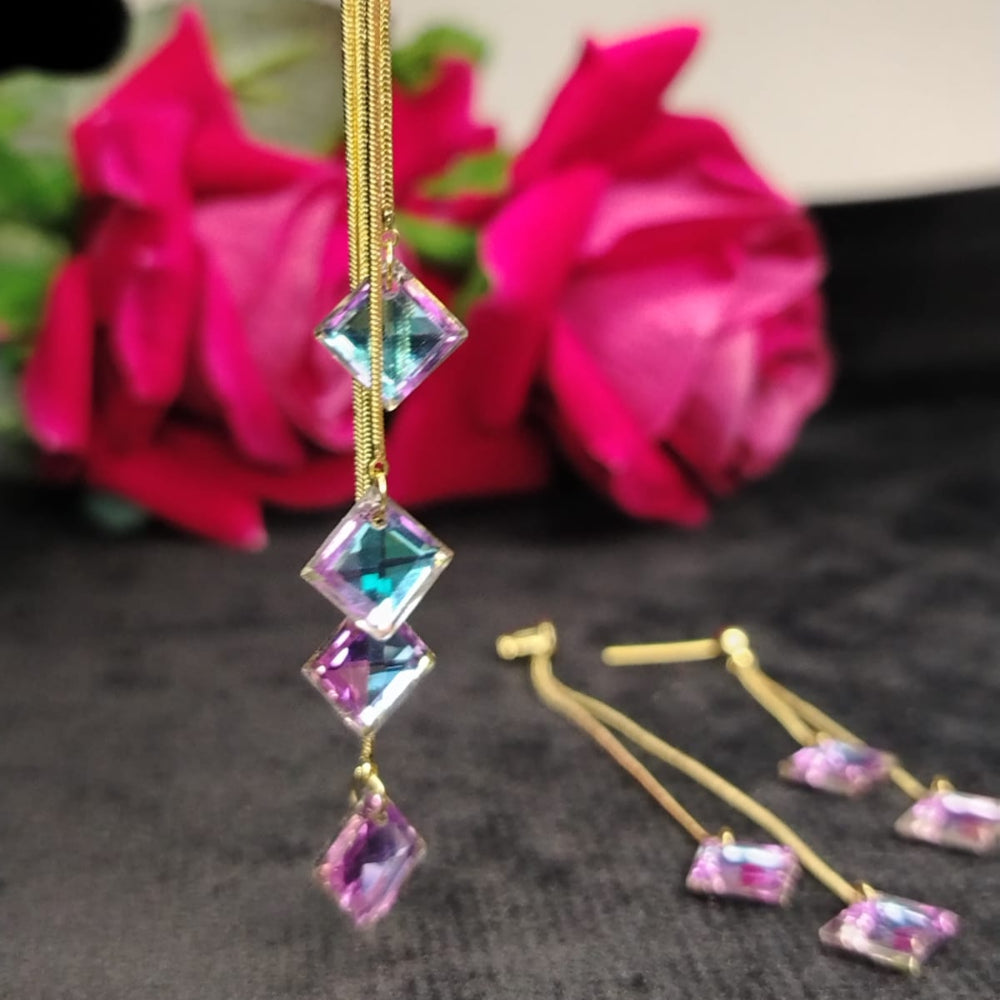 Gold earrings with colorful gemstones in front of pink flowers