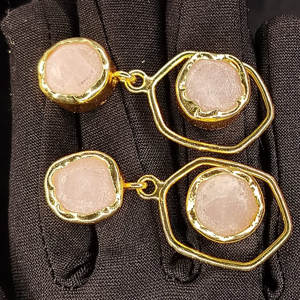Pair of gold-framed earrings with pink gemstones on a black glove background