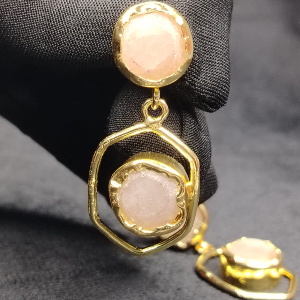 Gold and pink earrings held by a black gloved hand on a dark background