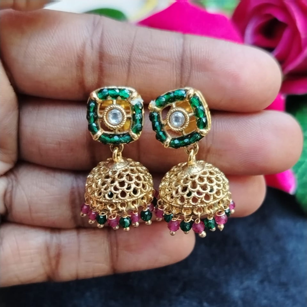 Gold earrings with green and red stones held between fingers against a dark background
