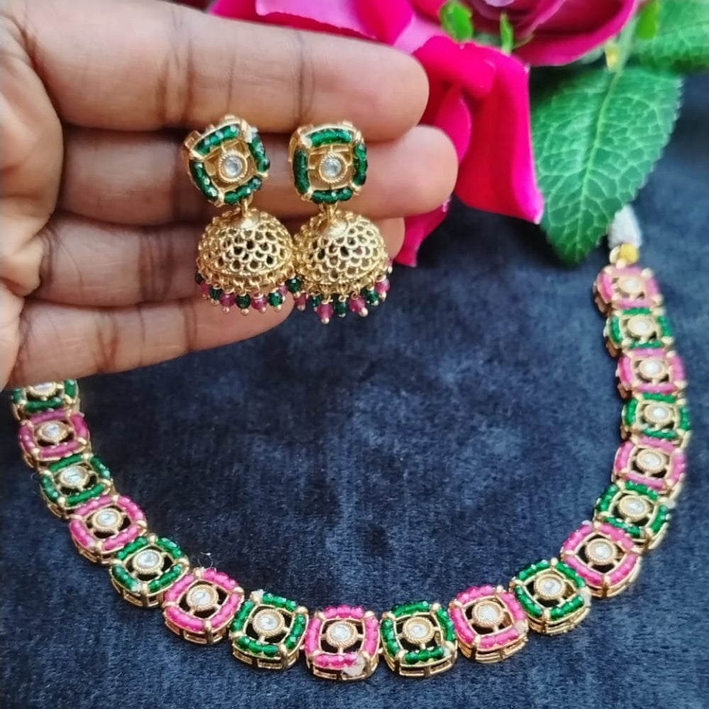 Gold necklace with pink and green accents held by a hand, with a pink flower in the background.
