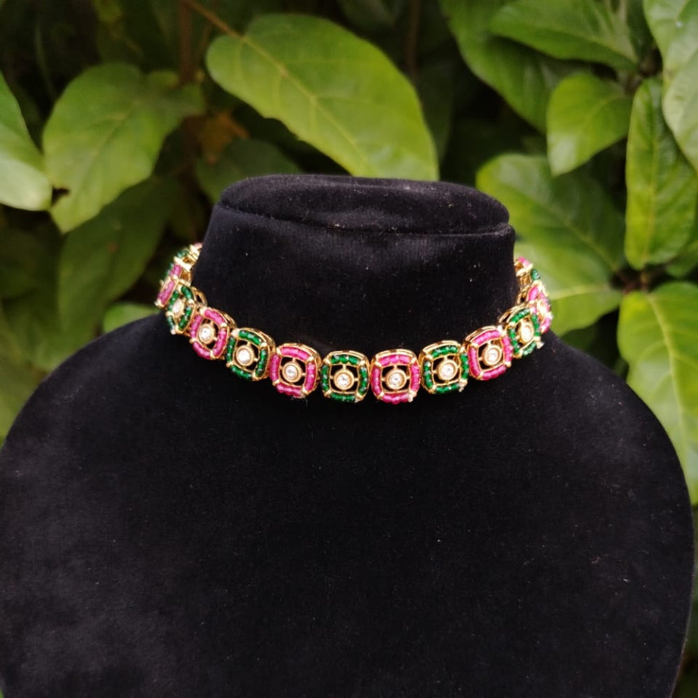Necklace with pink and green stones on a black velvet stand against a leafy green background