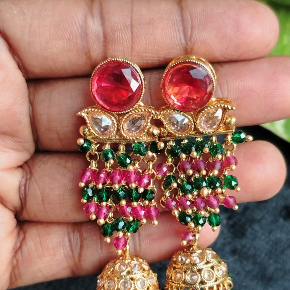 Ornate earrings with red and green gemstones held in a hand against a blurred background