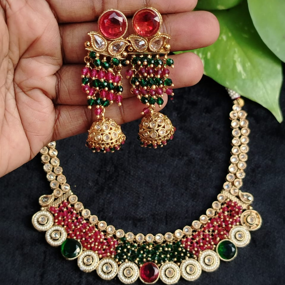 Gold necklace with red and green stones held by a hand against a dark background with green leaves.