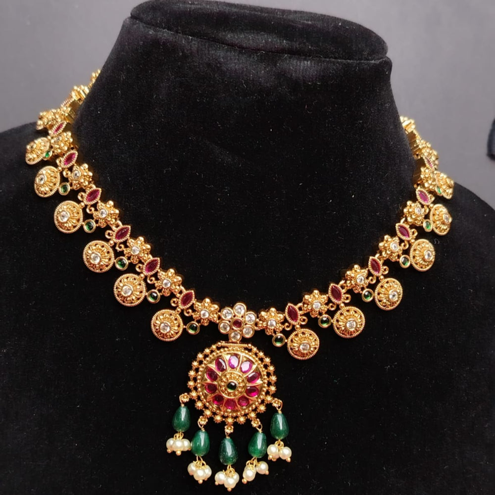 Ornate gold necklace with red and green stones on a black stand