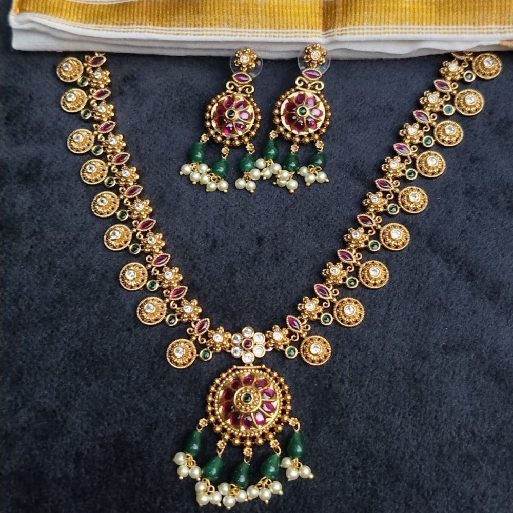 Gold necklace with green and red accents on a dark fabric background