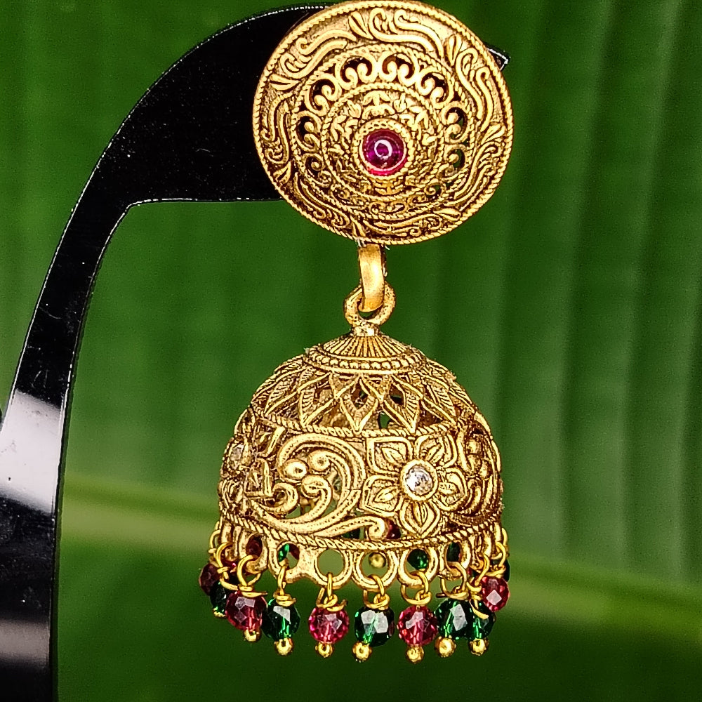 Golden jhumka earring with red and green stones on a green leaf background