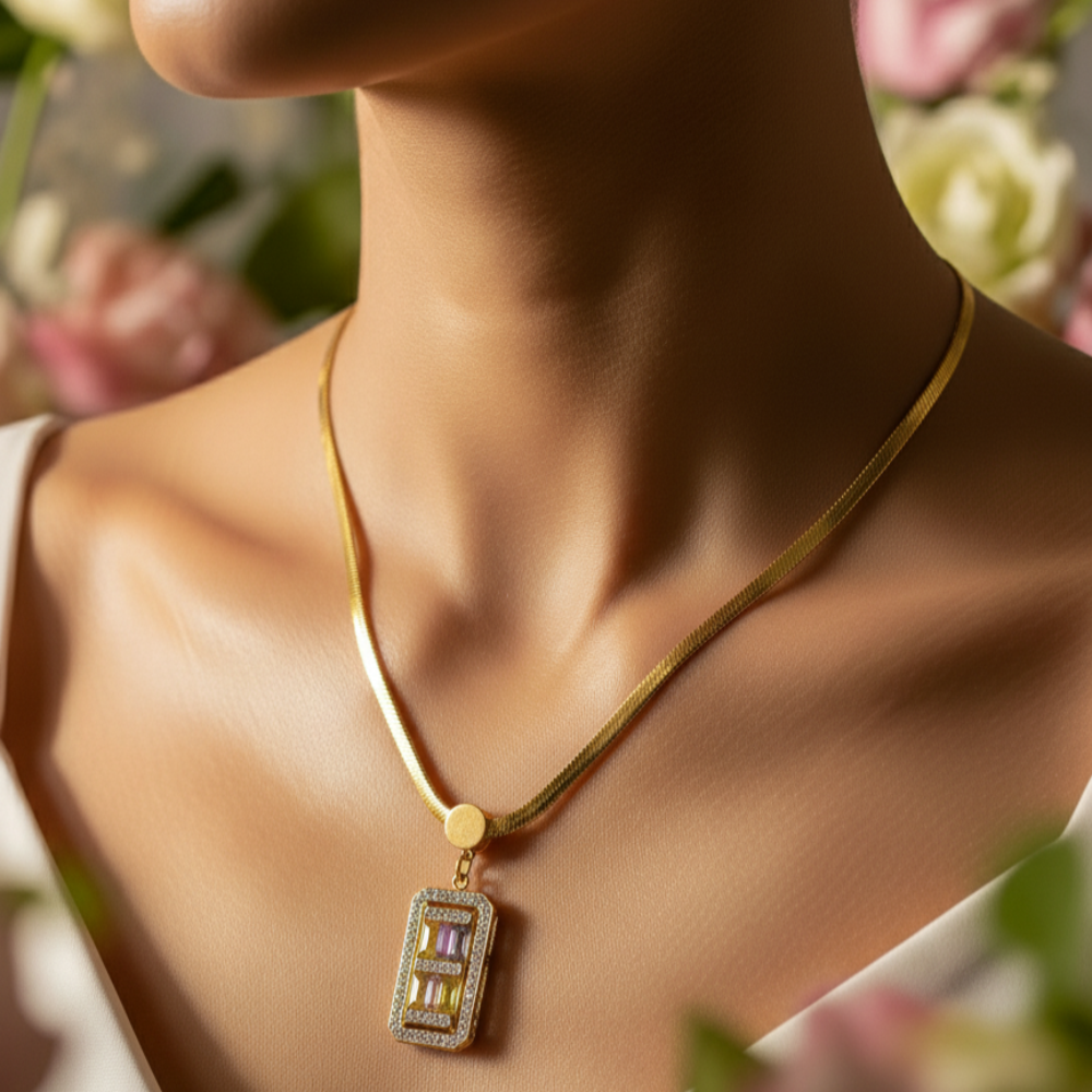 Gold necklace with a colorful pendant worn by a person, surrounded by flowers.