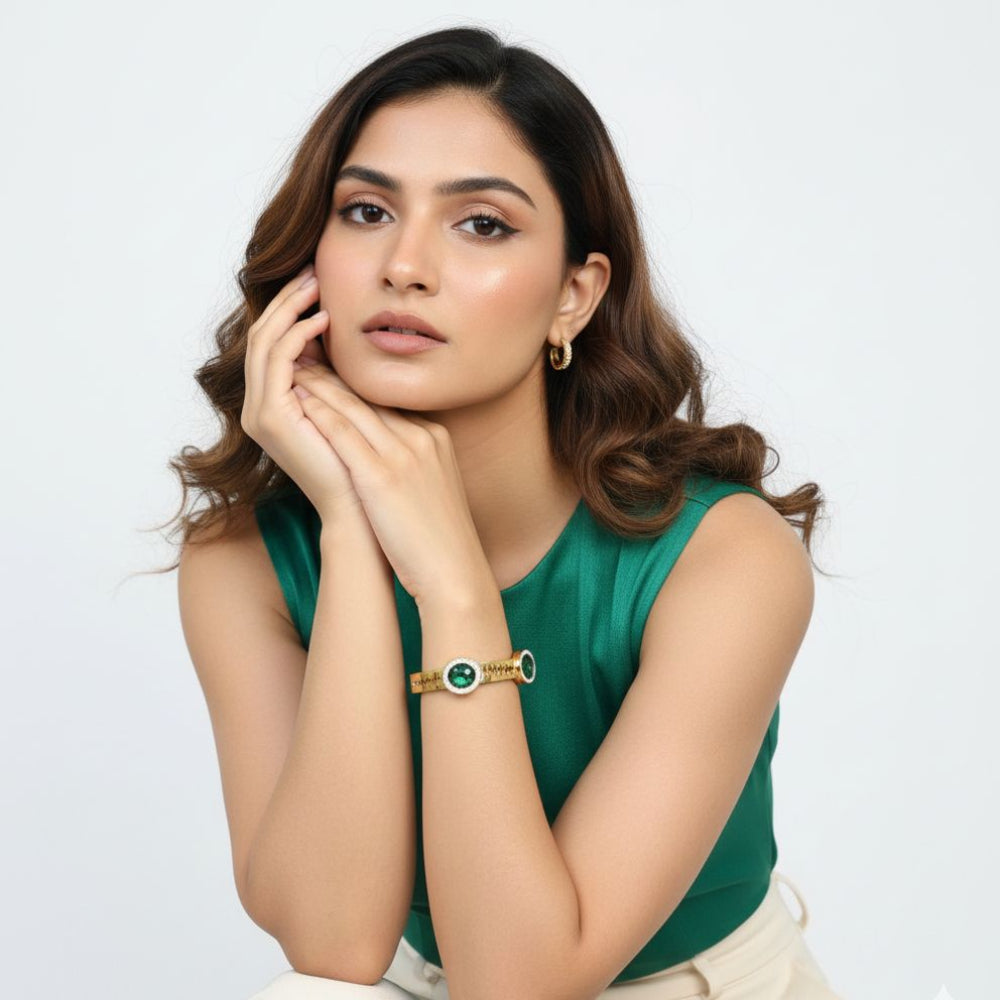 Woman wearing a green sleeveless top and a gold bracelet with green crystals on a white background