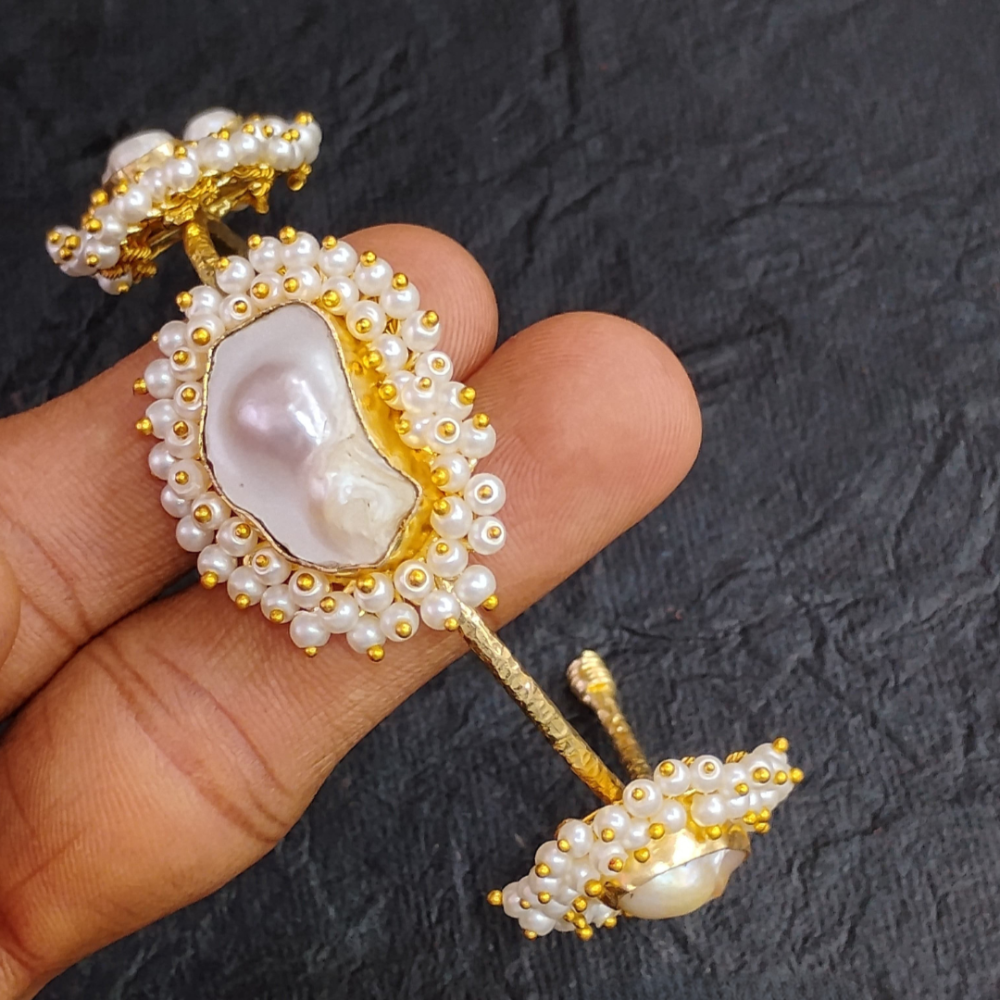 Golden and pearl bracelet held by a hand on a dark textured background
