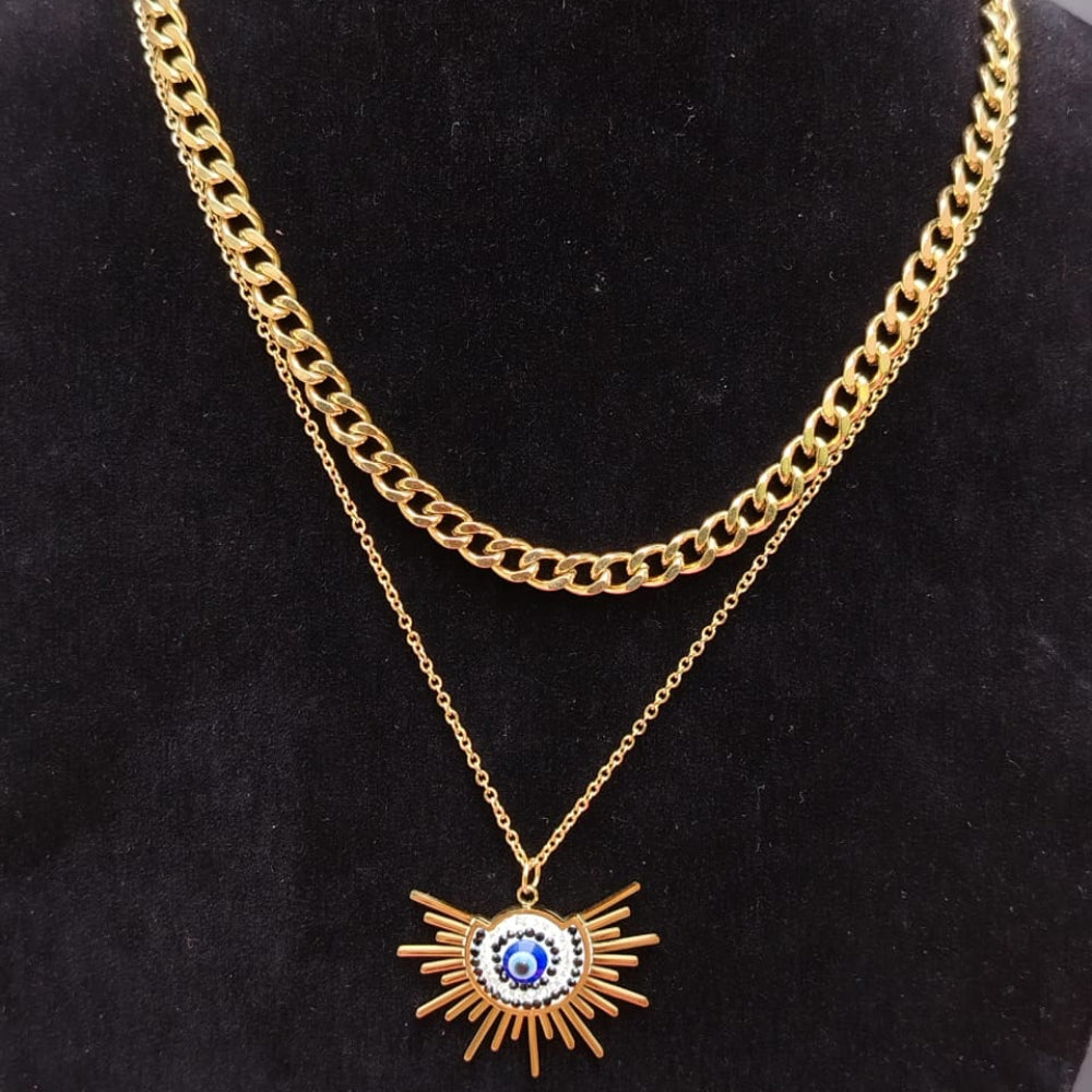 A double-layered gold necklace displayed on a black velvet jewelry bust. The top layer features a thick curb chain, and the bottom layer features a delicate chain with a gold sunburst pendant containing a blue evil eye design in the center.