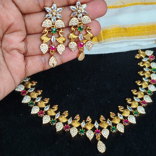 Gold necklace and earrings with gemstones held by a hand on a black surface.