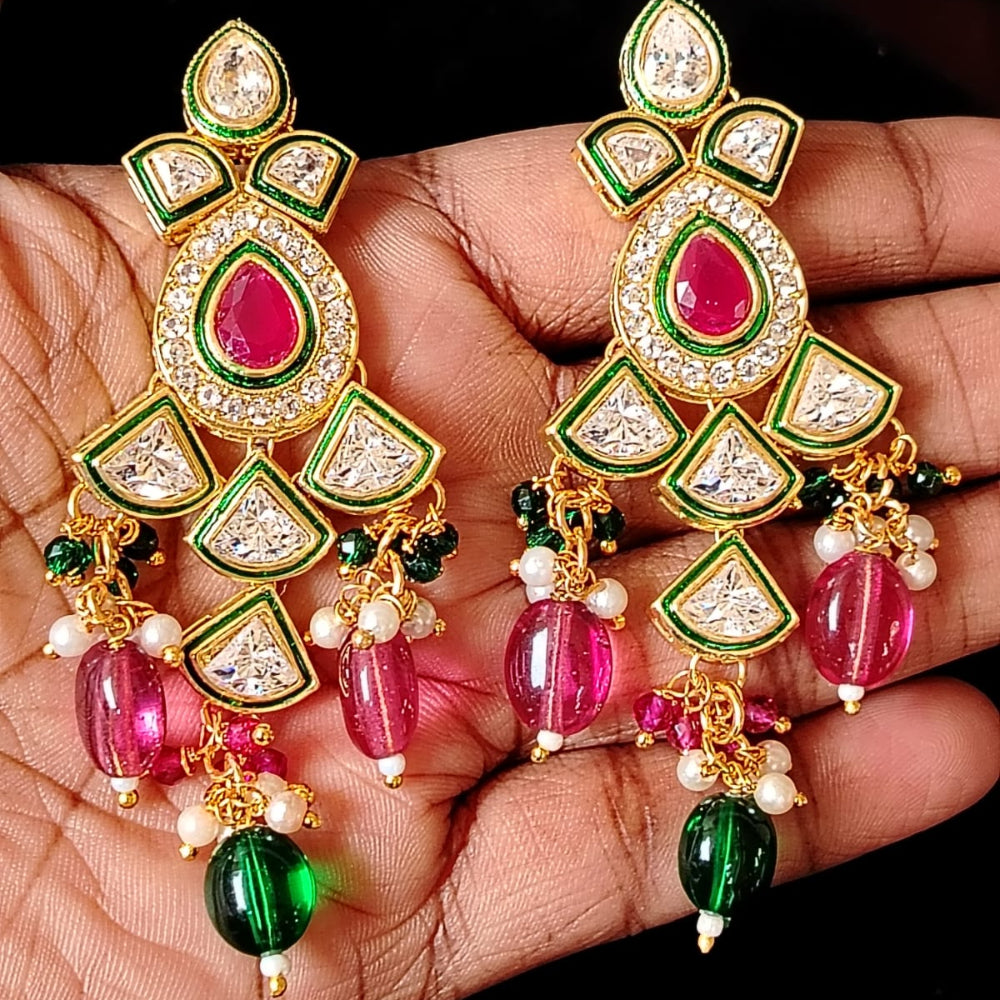 Ornate earrings with pink and green stones held in a hand against a dark background