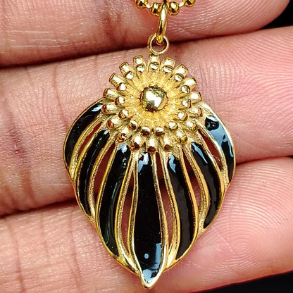 Gold and black pendant held between fingers with a blurred red background