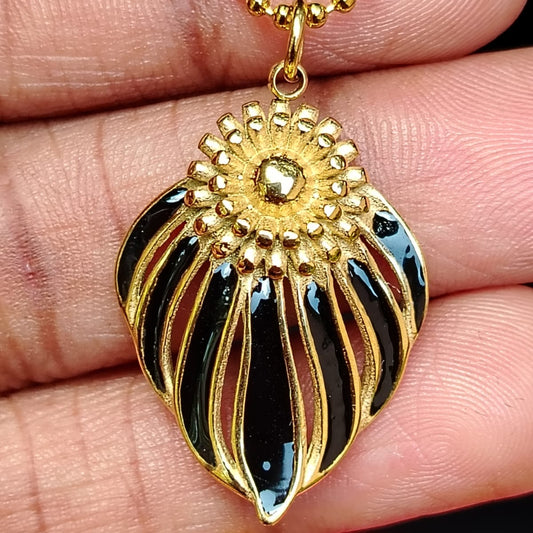 Gold and black pendant held between fingers with a blurred red background