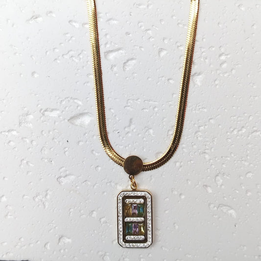 Golden necklace with a rectangular pendant on a textured white surface