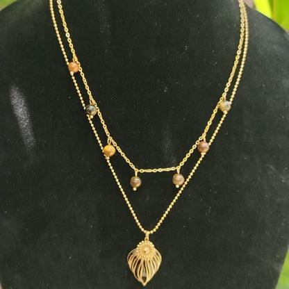 Gold necklace with leaf pendant on a black mannequin bust with green foliage in the background