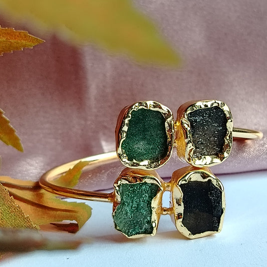 Golden Bracelet  with Green and Black Gemstones on a light Pink Fabric Background