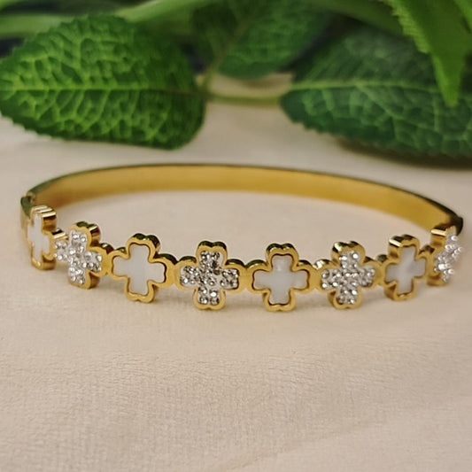 Clover Motif Anti-tarnish Bracelet on a Beige Surface with Green Leaves in the Background