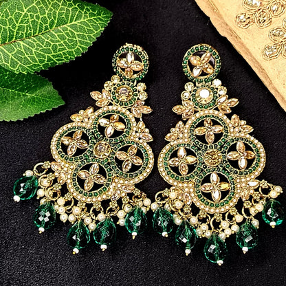 Ornate Gold and reen earrings on a Black Surface with Leaves and Fabric in the Background