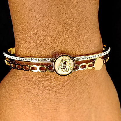 Gold bracelet with a circular emblem on a wrist against a black background