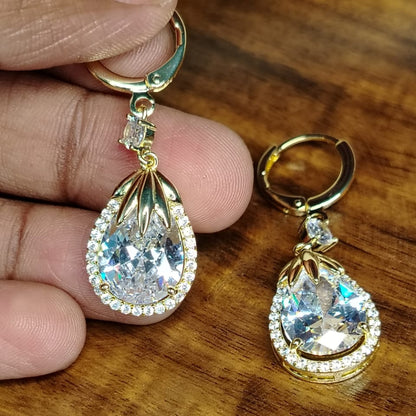 Golden American Diamond Tear Drop Hoops Held By Hands against Wooden Background