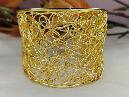 Gold Plated Broad Filigree Bracelet against a Blurred Background