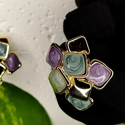 Multicored Eanamel Square Design Earrings with Gold Accents Held by a Gloved Hand
