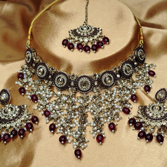 Golden Ornate Jewellery Set with Maroon Beads and Kundan on a Beige Background
