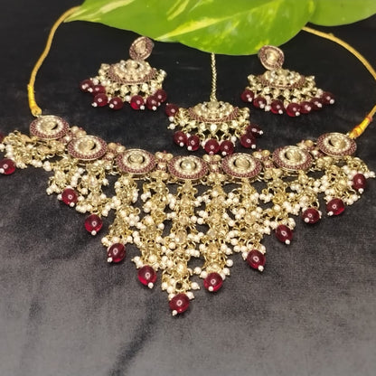 Golden Ornate Jewellery Set with Maroon Beads and Kundan on a Black Surface